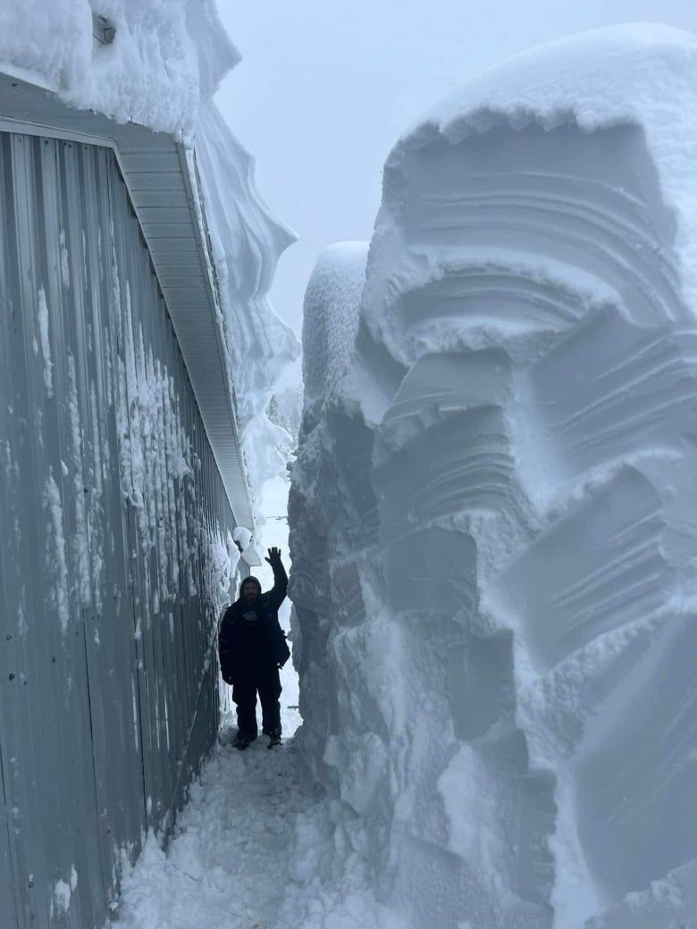 A man stands between a barn and a 4 metre snow bank.