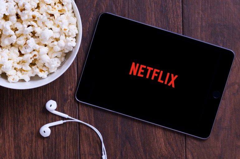 New York, USA - October 12, 2018: Table with popcorn bottle and Netflix logo on Apple Ipad mini and earphone. Netflix is a global provider of streaming movies and TV series.