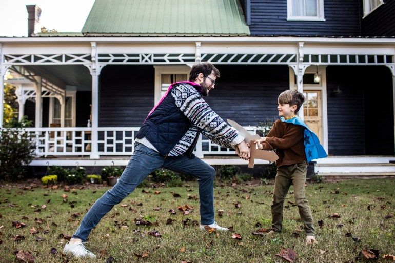 Father and son playing with cardboard swords in front of farmhouse